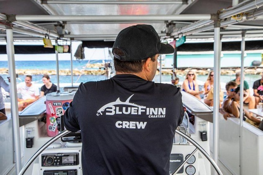 A person wearing a 'Bluefin Crew' shirt on a boat, steering the vessel. 5