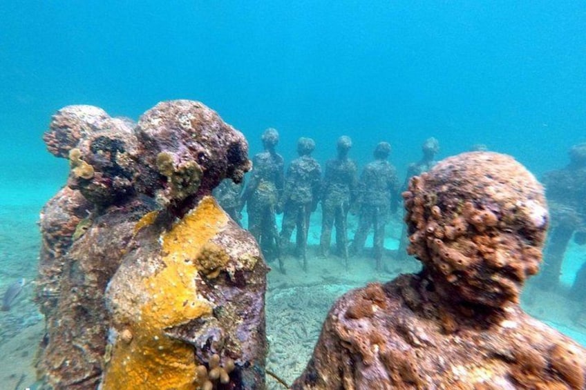 Underwater sculptures of human figures, likely memorials, surrounded by marine growth. 4