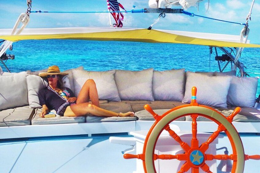 A person lounging on a boat's deck with a steering wheel and a flag in the background. 2