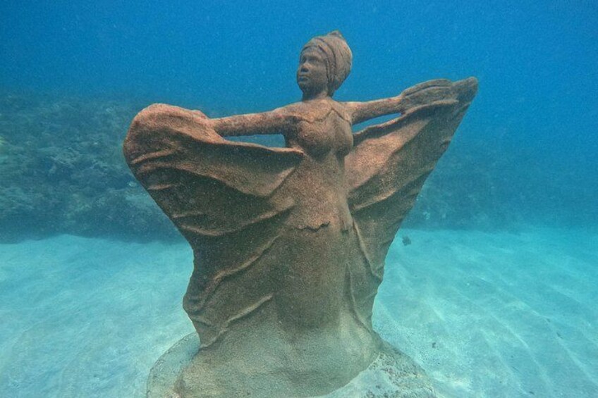 A submerged statue with outstretched arms, surrounded by clear blue water. 2