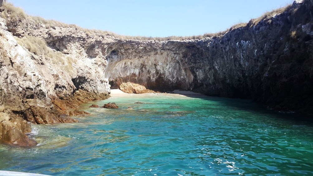 A coastal cave with turquoise water and rocky cliffs. 1