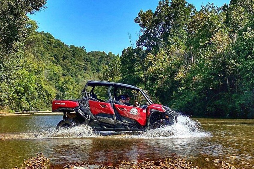 Un vehículo todo terreno rojo cruzando un río rodeado de un bosque denso. 3