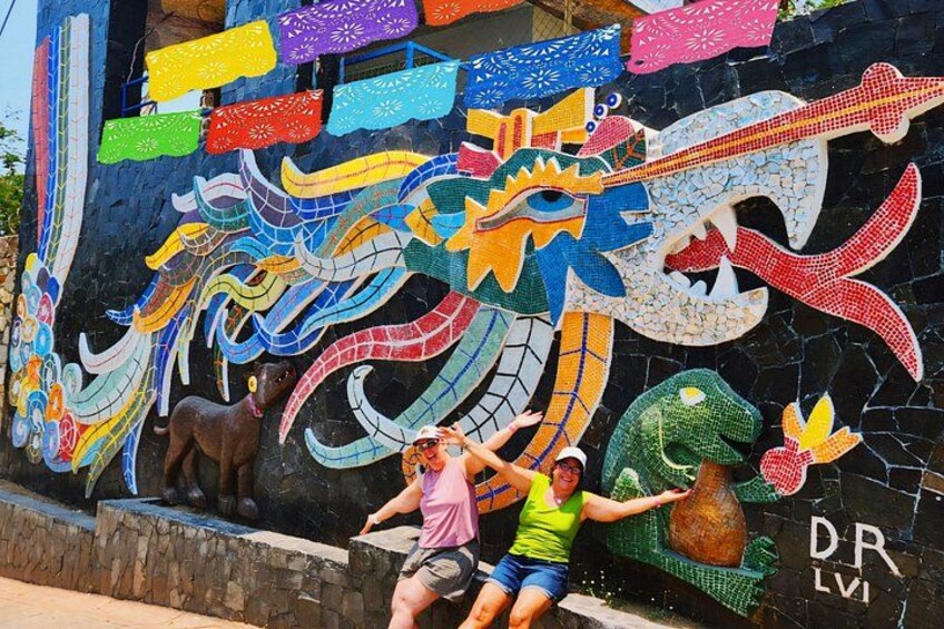 A colorful mural with a dragon and other figures, a stone wall, and a person sitting on a ledge. 1