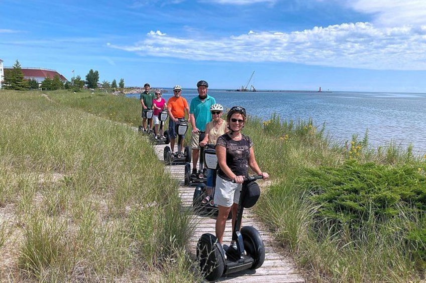 Eine Gruppe von Menschen fährt mit Segways auf einer Promenade entlang des Wassers. 1