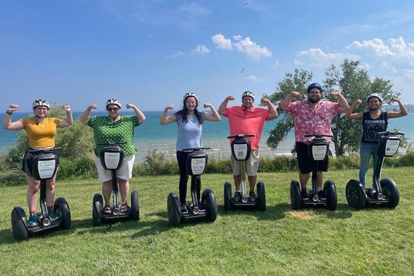 Eine Gruppe von Personen auf Segways posiert mit erhobenen Armen, im Hintergrund ist Wasser und Grünpflanzen zu sehen. 2