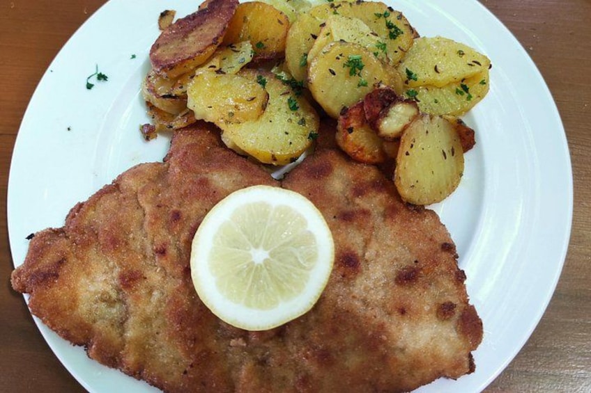A plate with a breaded cutlet, lemon, and roasted potatoes. 5