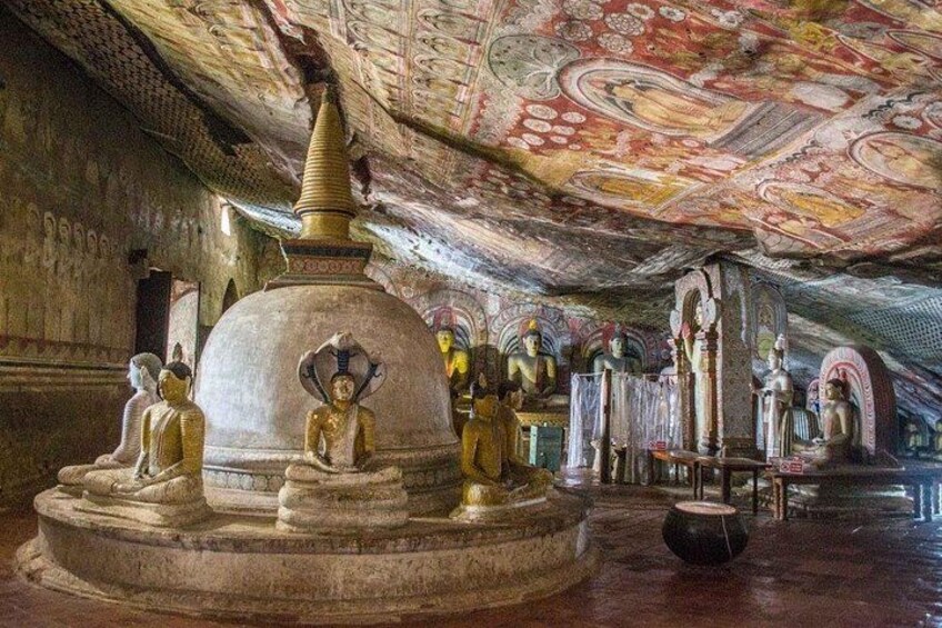 A temple interior with a large stupa, seated Buddha statues, and intricate ceiling artwork. 1