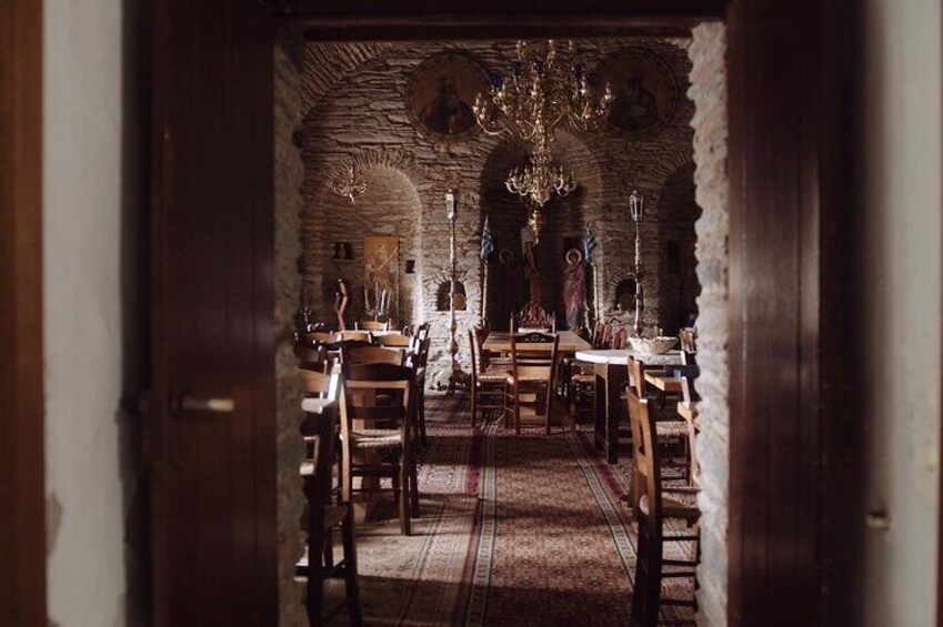 A medieval dining hall with stone walls, wooden tables, and a chandelier. 1