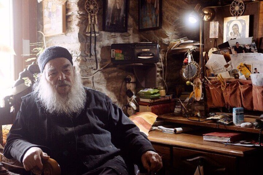 A person sitting in a room with a rustic stone wall, a desk with papers and a lamp, and various personal items. 2