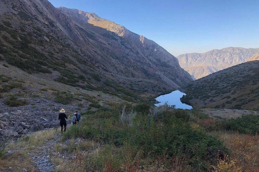A mountainous landscape with a small lake, rocky terrain, and hikers in the distance. 3