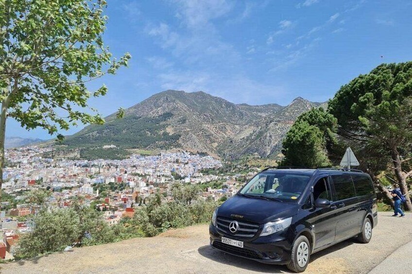 Un fourgon noir est garé sur une route, avec un paysage montagneux et une ville en arrière-plan. 2