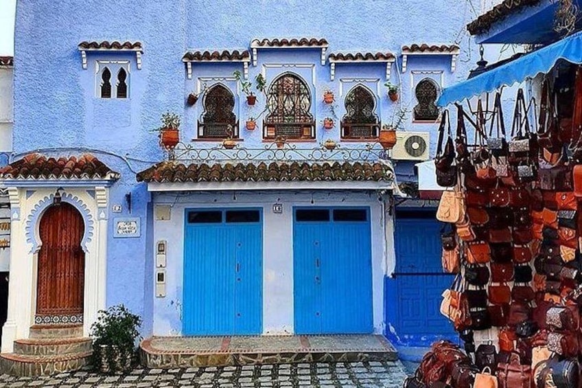 A blue building with a blue door, a tiled roof, and a shop selling bags. 2
