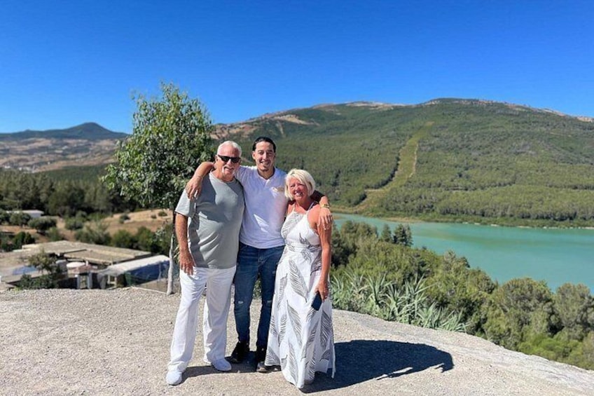 Trois personnes se tiennent debout sur un promontoire rocheux, avec un lac et des collines en arrière-plan. 4