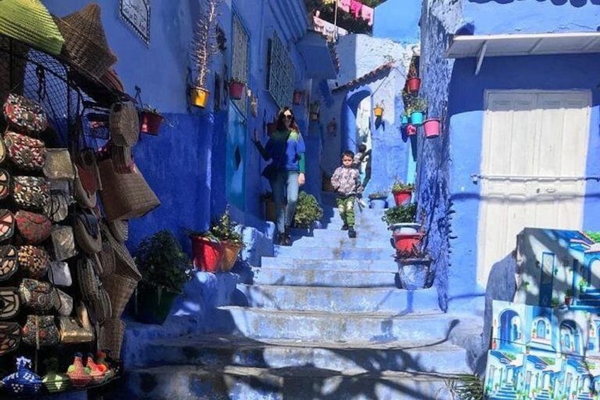 A narrow street with blue buildings, steps, and hanging baskets. 3