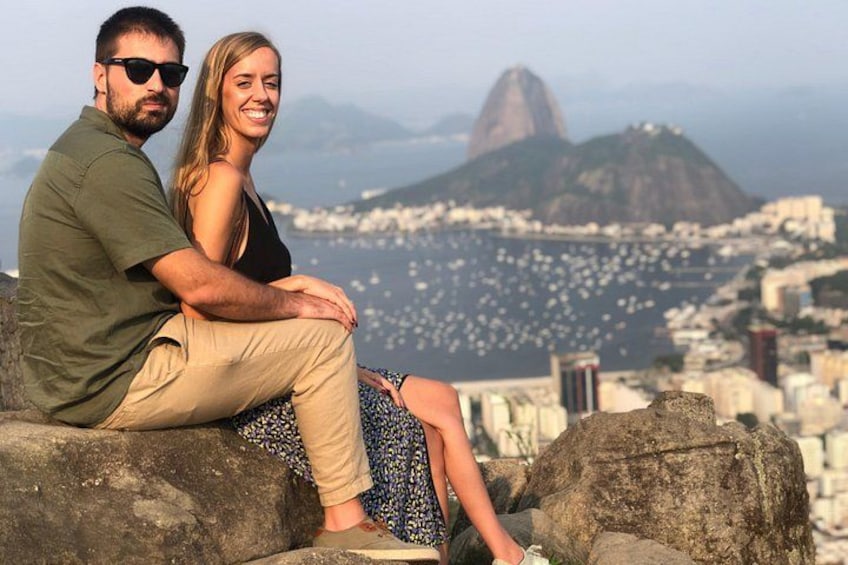 A couple sitting on rocks with a cityscape and a mountain in the background. 1