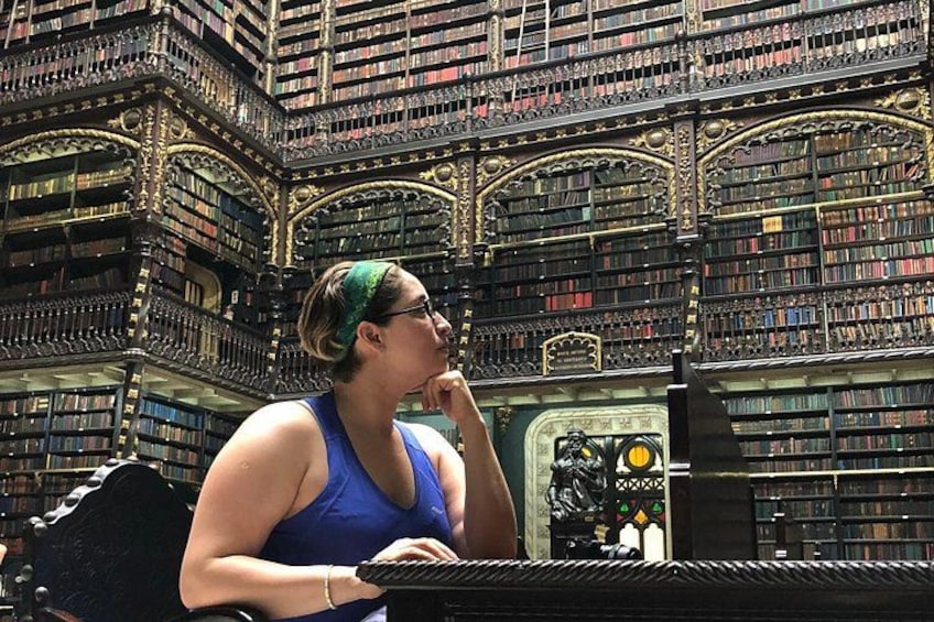 A person in a blue tank top sitting at a piano in a library with ornate bookshelves. 5