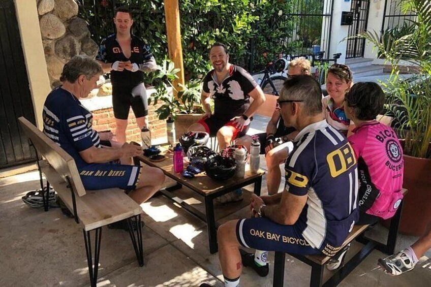 Un grupo de personas sentadas en una mesa al aire libre, con bicicletas y equipo de ciclismo. 3