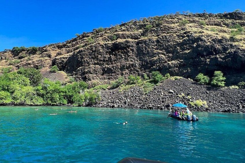 A river with clear blue water, a boat with passengers, and a rocky hillside in the background. 2