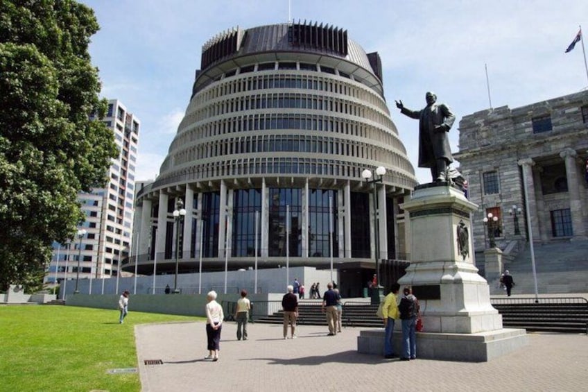 A modern building with a curved facade, a statue in front, and people walking around. 3