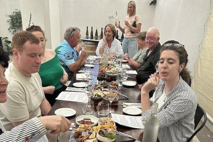 A group of people seated around a long table with food and drinks, engaged in conversation. 2