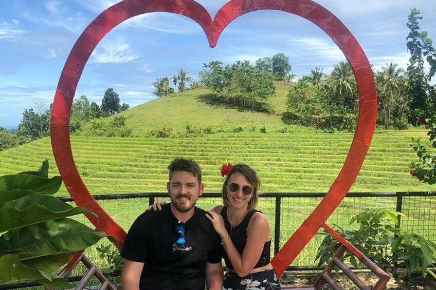 Eine herzförmige Struktur vor einer grünen Landschaft, mit einer Person und einem Kind davor. 2