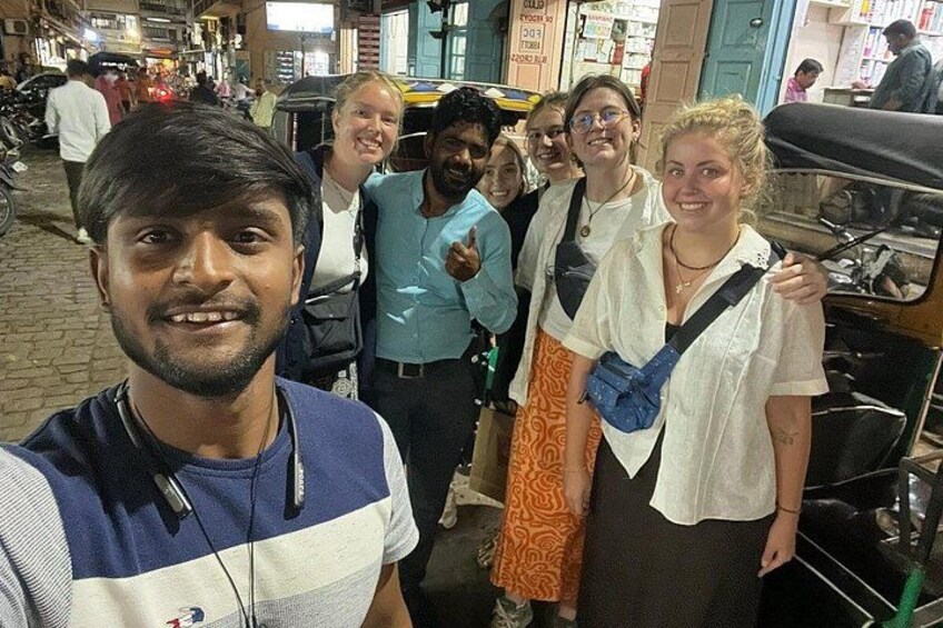 Un grupo de personas de pie en una calle con tiendas y vehículos al fondo. 2