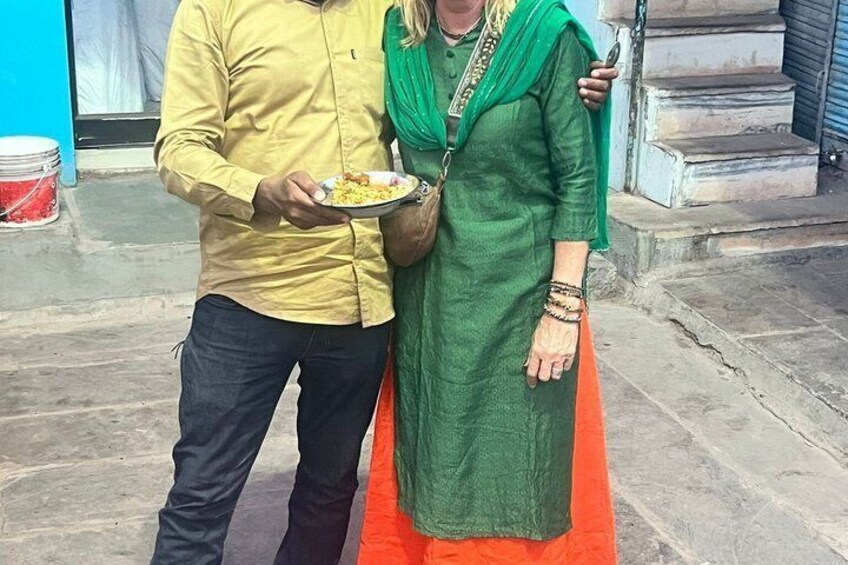 Une personne portant un t-shirt jaune tient une assiette de nourriture et se tient à côté d’une autre personne vêtue d’une robe verte et d’un châle orange. 1