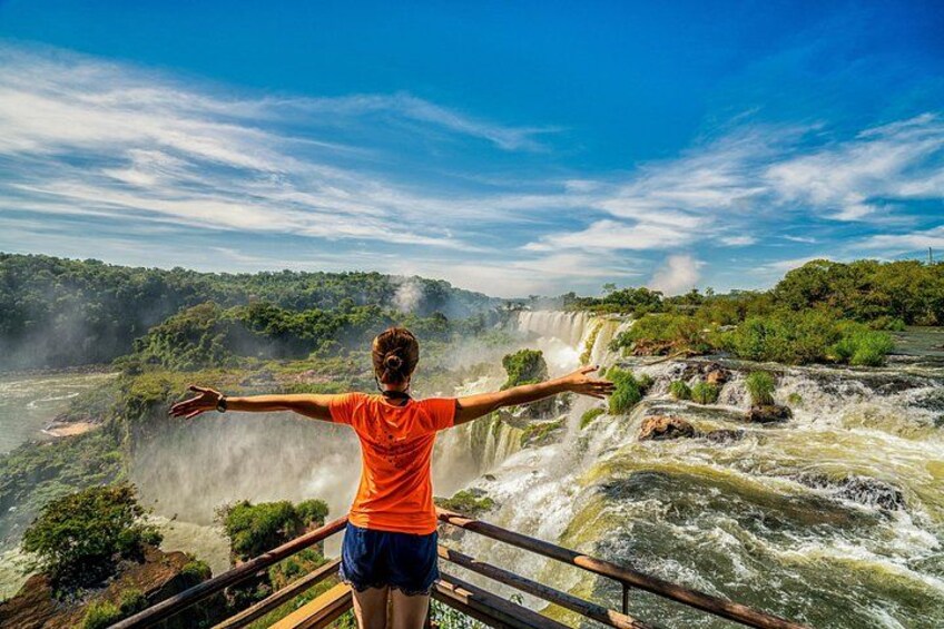 A person standing on a bridge with arms outstretched, overlooking a waterfall. 1