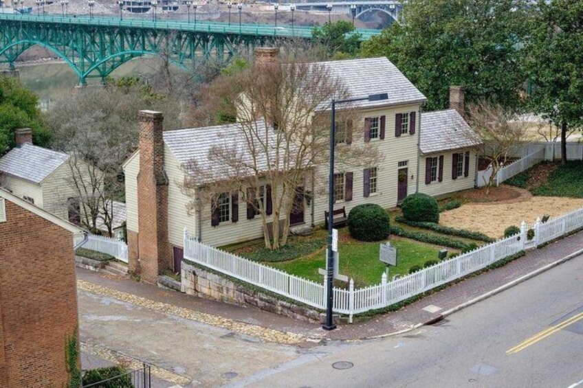 Ein historisches Haus mit weißem Zäunchen, einem Backstein-Schornstein und einer grünen Metallbrücke im Hintergrund. 5