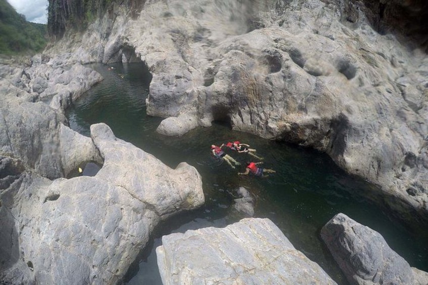 A group of people swimming in a natural rock pool surrounded by large boulders. 3