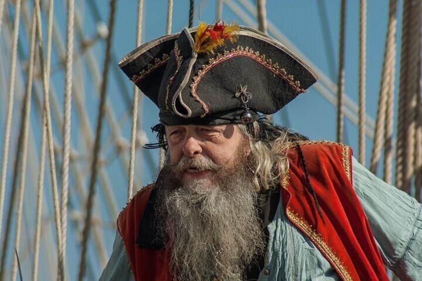 A person wearing a pirate hat with a red and gold trim, a blue shirt, and a red cloak. 2