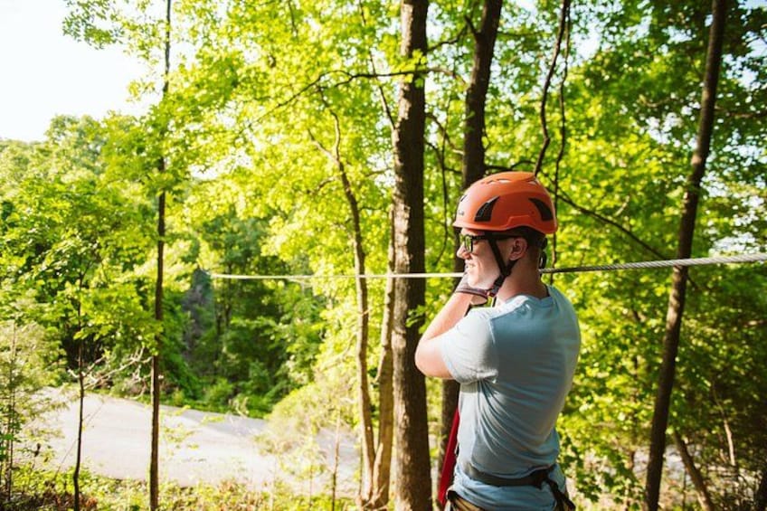 Une personne portant un casque et un harnais, sur une tyrolienne, entourée d’arbres. 5