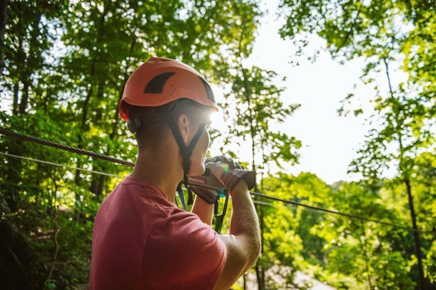 Une personne portant un casque et un harnais, se tenant sur un pont de corde entouré d’arbres. 4