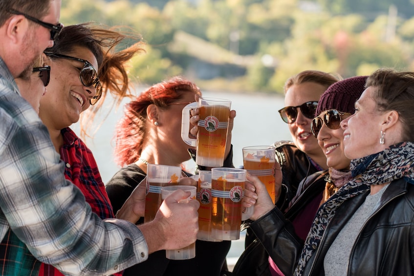 A group of people toasting with beer mugs by a lake. 1