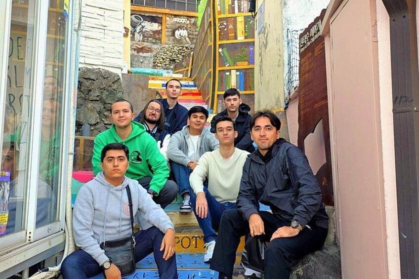 A group of people sitting on steps outside a building with bookshelves and a stone wall. 3