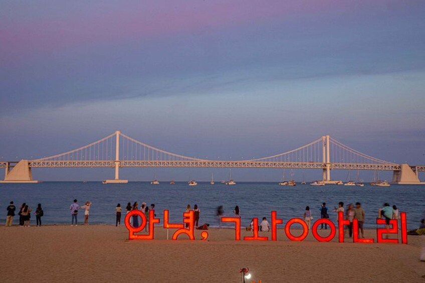 A bridge over water with people on the beach and boats in the distance. 2