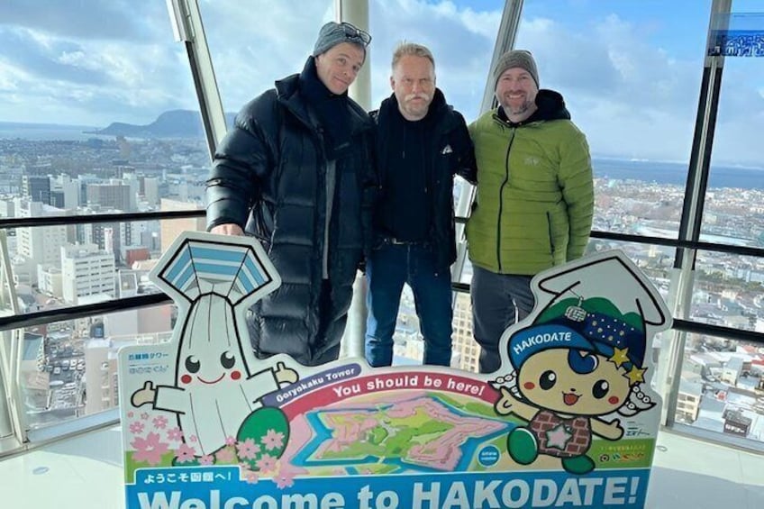 Three people standing in a high-rise building with a cityscape view. 1