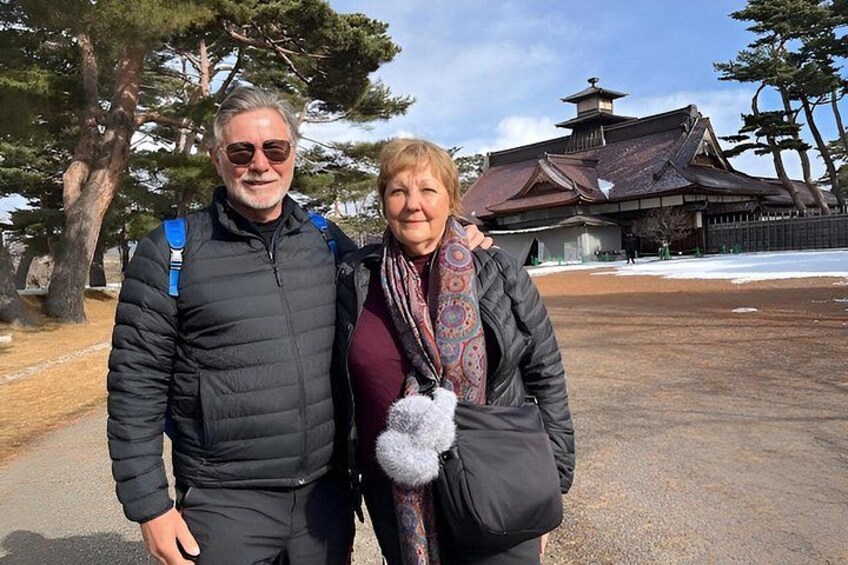 Two people standing in front of a traditional building with a snow-covered ground. 5
