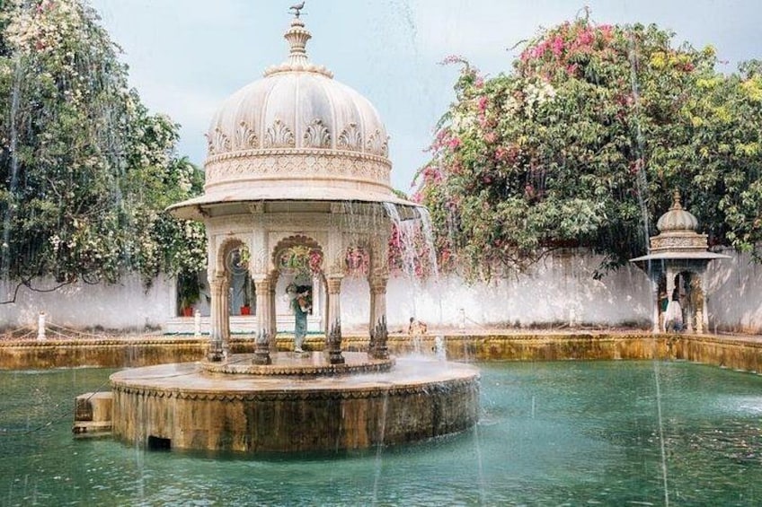 A water fountain with a gazebo, surrounded by lush greenery and flowering trees. 5