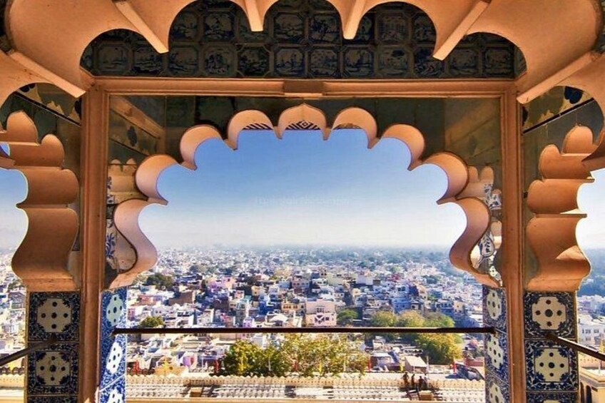 A view through a traditional archway with intricate blue and white patterns, overlooking a cityscape with buildings and greenery. 2