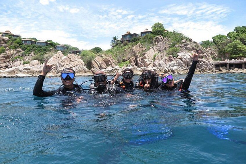 A group of divers in clear water with rocky terrain and vegetation in the background. 1