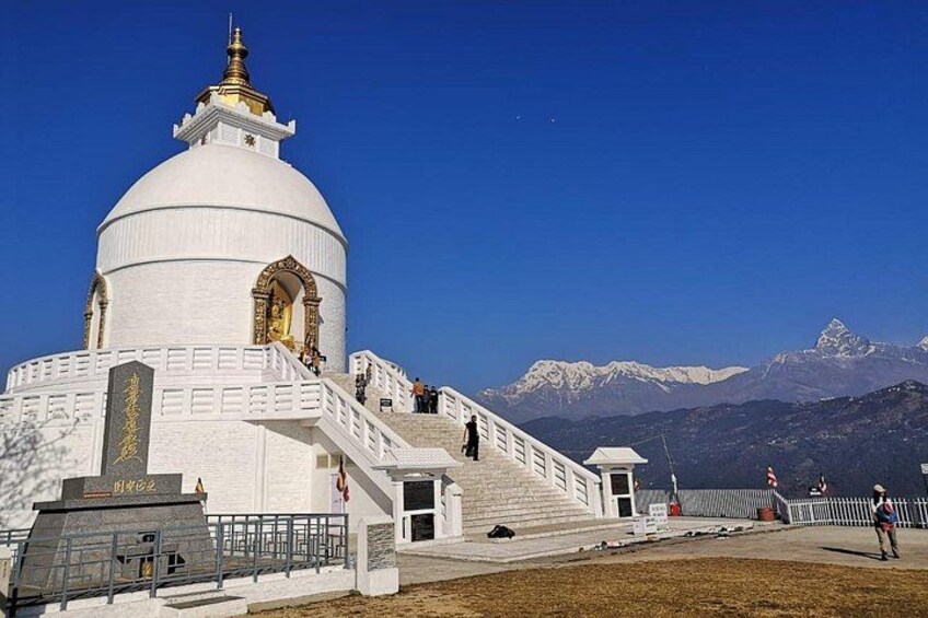 A white building with a golden dome, stairs leading up to it, and snow-capped mountains in the background. 1