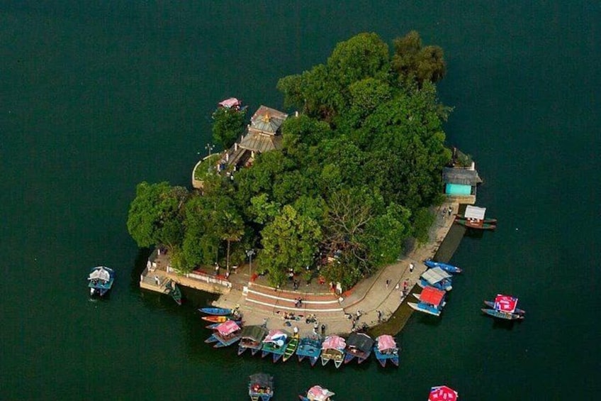 An aerial view of a small island with dense greenery, a dock with boats, and a few buildings. 1