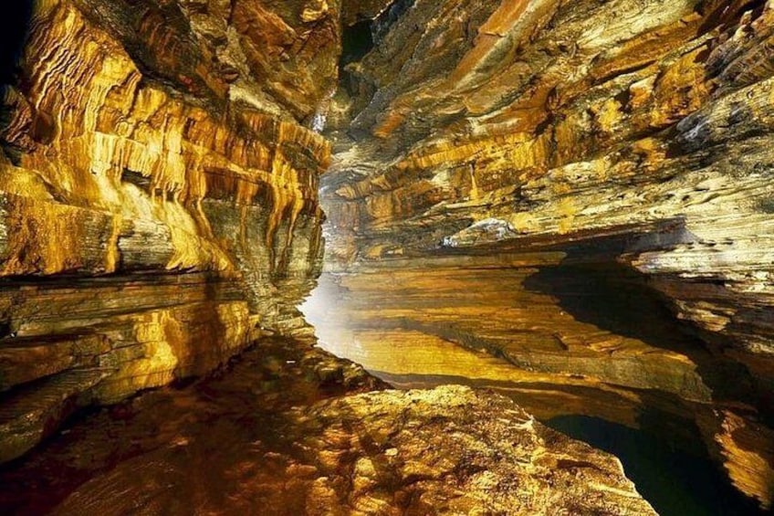 A cave with golden rock formations and a reflective water surface. 5