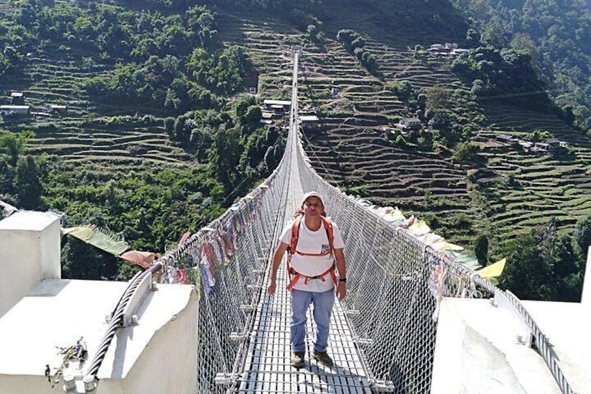 Une personne se tient sur un pont suspendu, avec des champs en terrasses en arrière-plan. 4