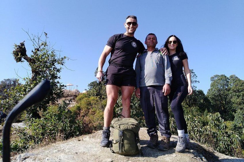 Trois personnes se tiennent sur un sentier rocailleux, portant un sac à dos et des chaussures de randonnée, entourées de verdure et sous un ciel dégagé. 1