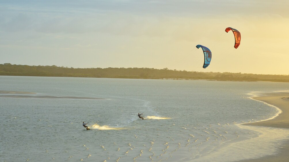 A beach with people windsurfing and two kites flying in the sky. 5