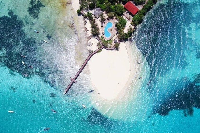 A beach with a pier, clear turquoise waters, and a small resort with a pool. 1