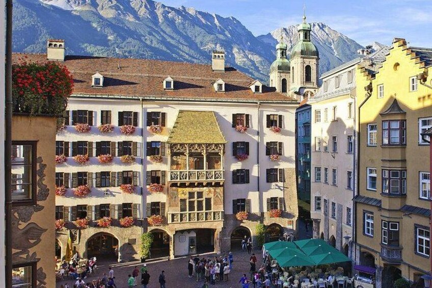 A square with buildings, a mountain in the background, and people walking. 2
