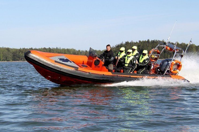 A red and black boat with four people wearing life jackets on the water. 1